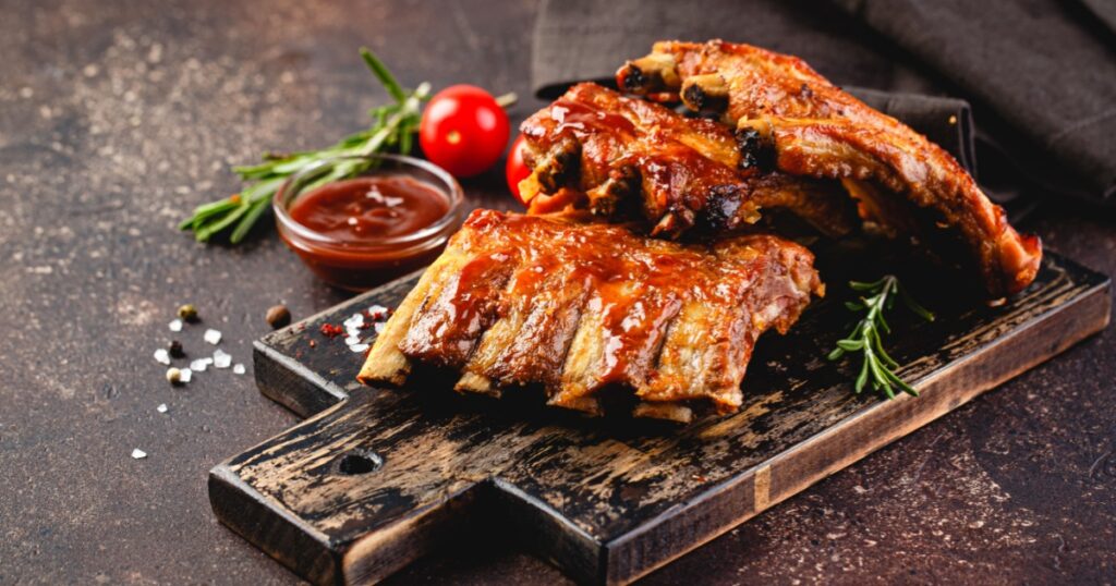 Grilled pork ribs on a wooden cutting board on a brown background