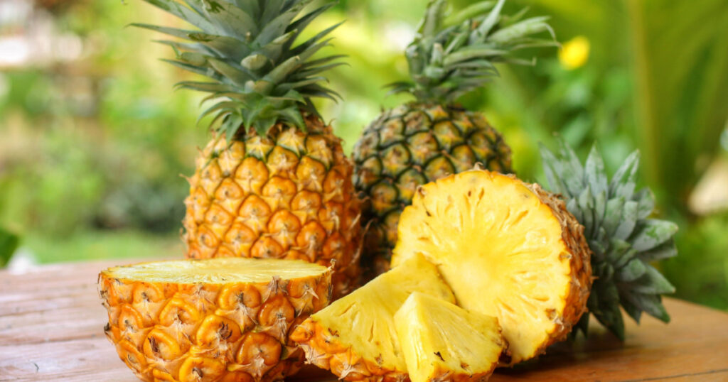 Sliced and half of Pineapple(Ananas comosus) on wooden table with blurred garden background.Sweet,sour and juicy taste.Have a lot of fiber,vitamins C and minerals.Fruits or healthcare concep