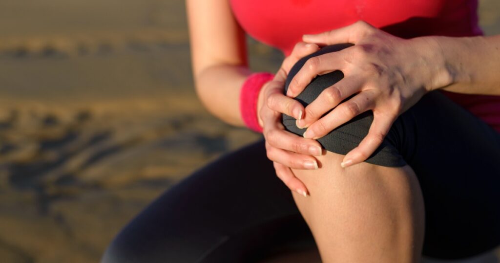Runner sport knee injury. Woman in pain while running in beach.