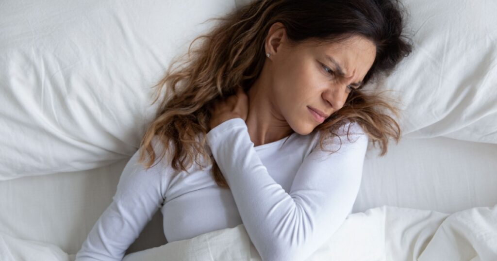 Above view frown millennial woman feels pain in neck after night, awaken in bad temper having painful sudden ache or stiffness, concept of poor incorrect posture during sleeping or too soft mattress