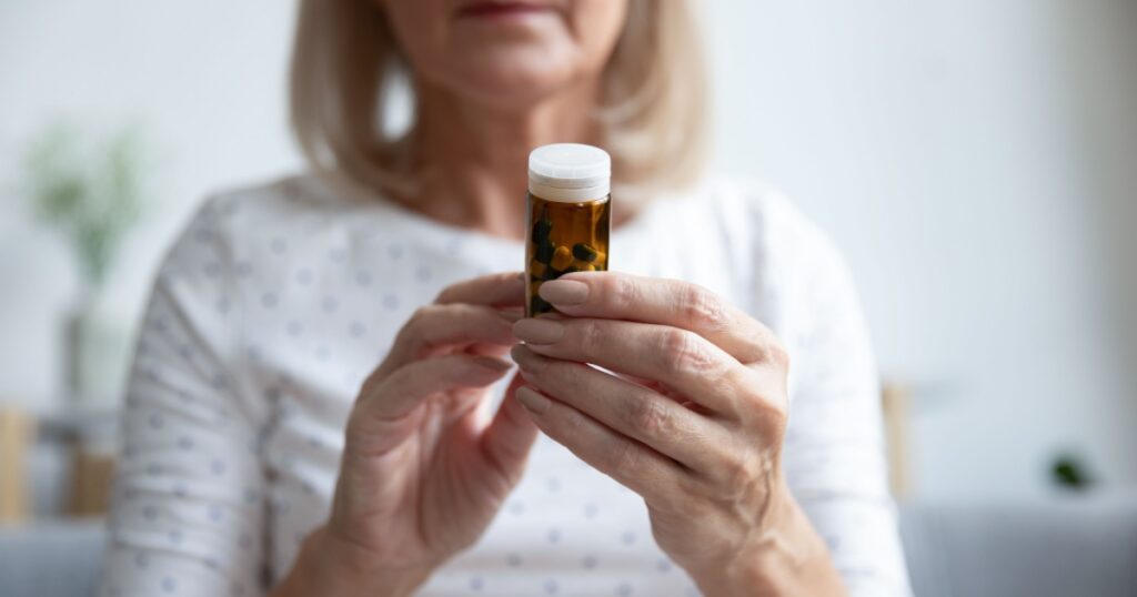 Elderly woman holding bottle of pills close up focus on female hands and capsules. Concept of herbal and natural remedies vitamins and minerals for older people, healthcare and pharmacy treatments