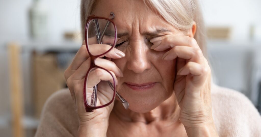 Close up of unhealthy elderly woman take off glasses massage eyes suffering from strong migraine or headache, unwell sick senior female grandmother struggle with blurry vision or dizziness