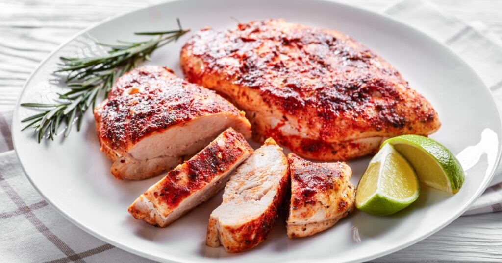 Healthy dish: grilled chicken breasts served on a white plate with fresh rosemary and lime on a white wooden background, close-up