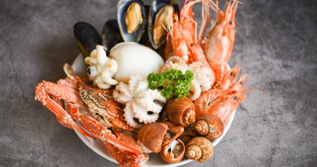 Seafood shrimps prawns squid mussels spotted babylon shellfish crab on plate and dark background / Cooked food served seafood buffet concept
