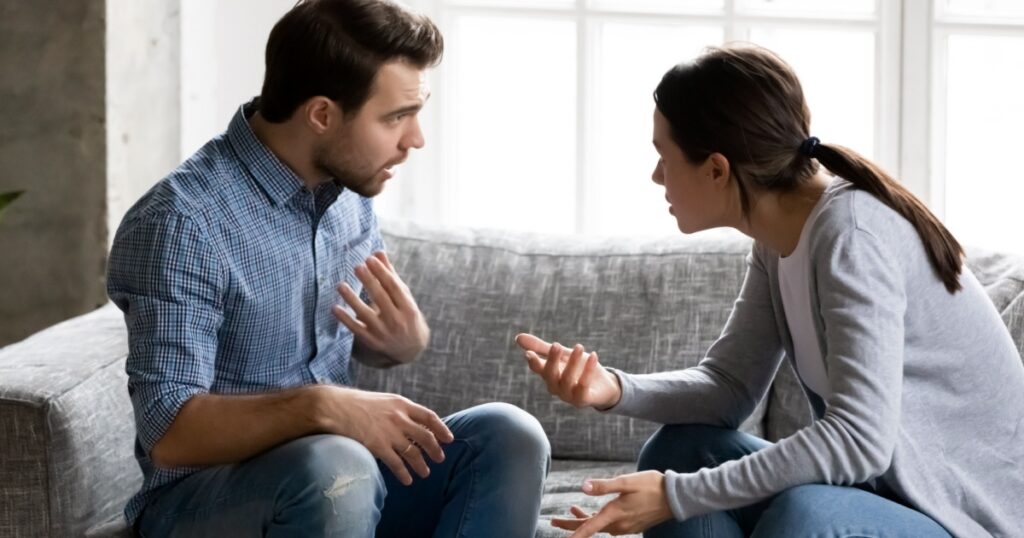 Stressed young married family couple arguing emotionally, blaming lecturing each other, sitting on couch. Depressed husband quarreling with wife, having serious relations communication problems.