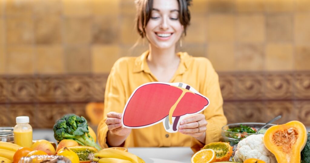 Woman holding human liver model with variety of healthy fresh food on the table. Concept of balanced nutrition for liver health