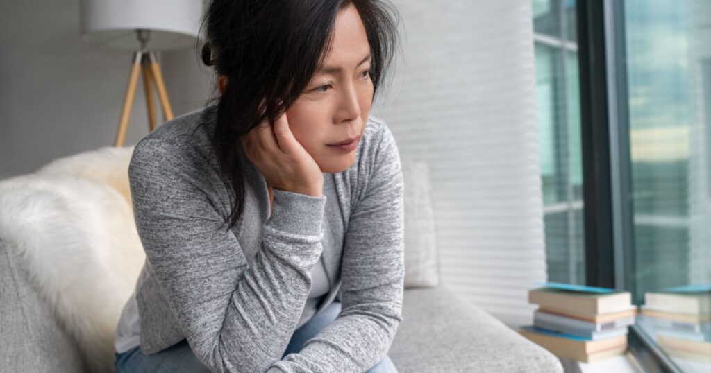 Sad Asian mature woman lonely at home self isolation quarantine for COVID-19 Coronavirus social distancing prevention. Mental health, anxiety depressed thinking senior chinese lady.
