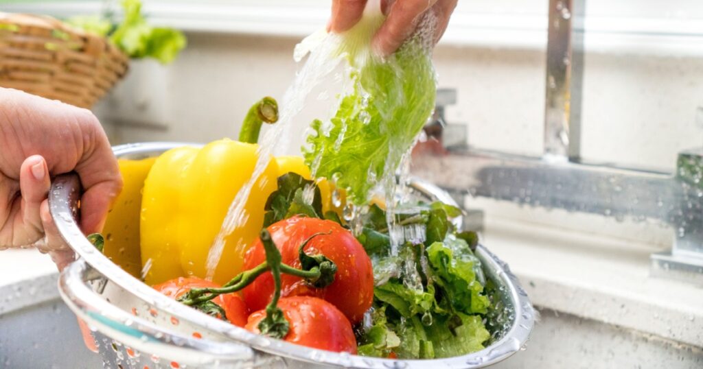 hands washing vegetables ( peppers, lettuce and tomatoes ) at home kitchen