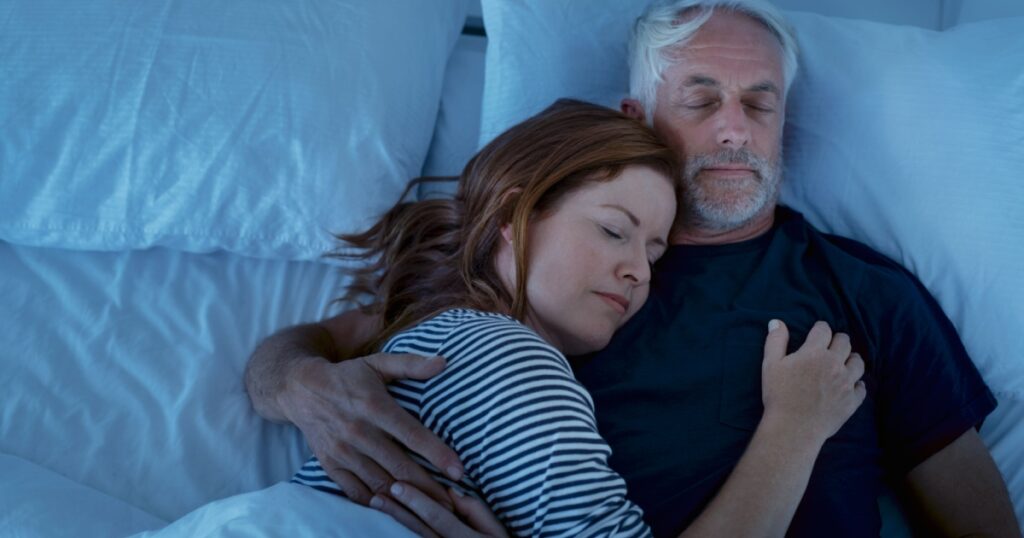 Senior man and woman sleeping and dreaming together in a deep sleep. Mature woman embracing and sleeps on her husband's chest while sleeping at night. Loving couple resting in their bed, copy space.