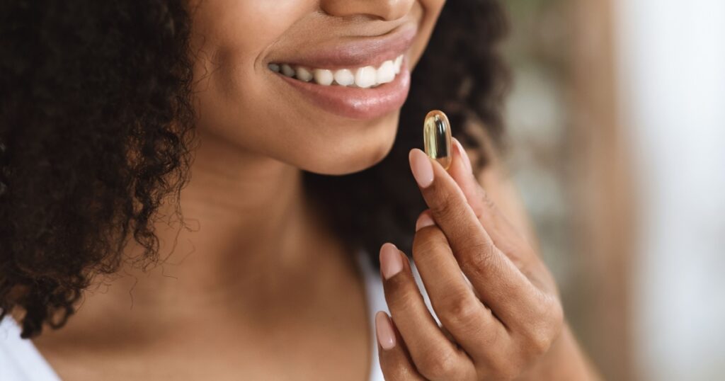 Beauty Supplement. Closeup Of Smiling Black Woman Taking Vitamin Pill Capsule, Having Diet Nutrition, Cropped Image