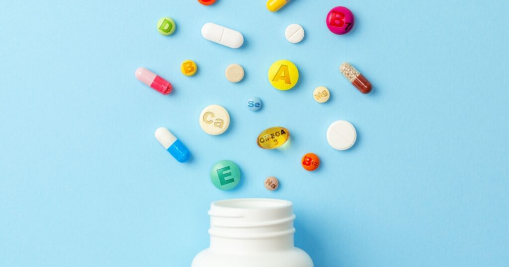 Vitamin tablets. Bottle with colored pills on blue background. Multivitamins.