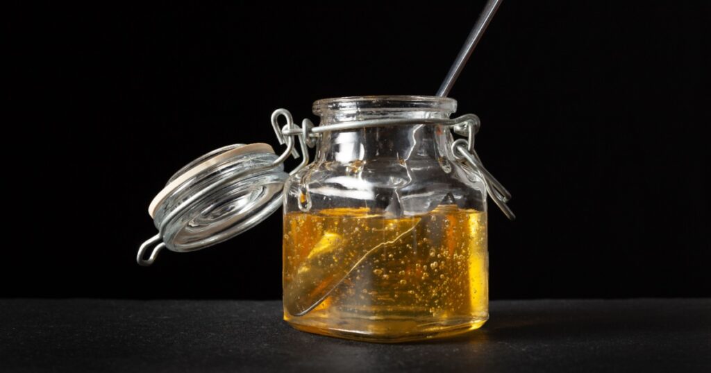 agave syrup in glass jar with spoon inside. black background