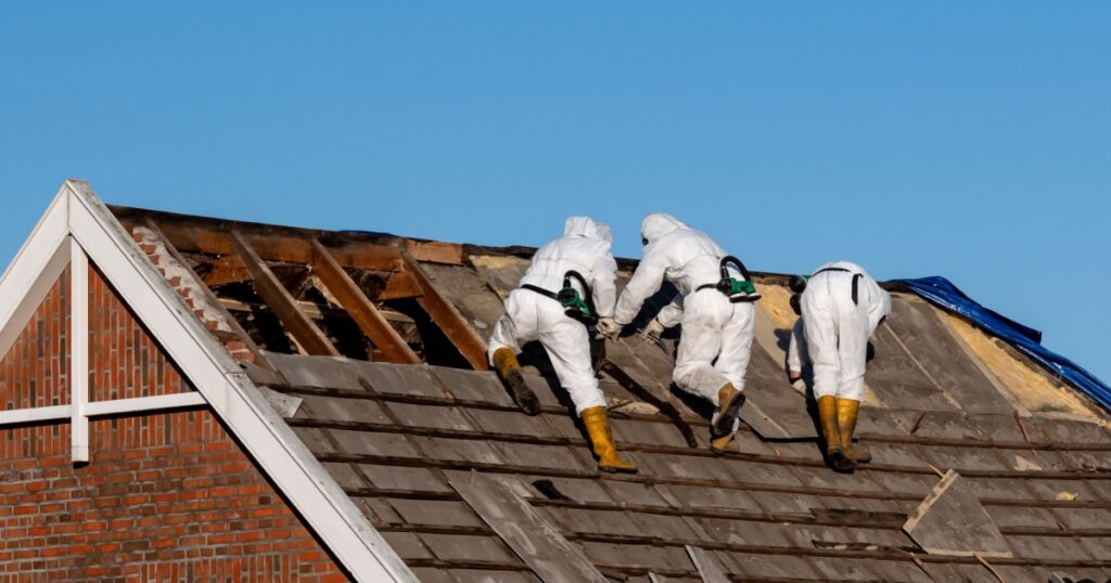 Professionals in protective suits remove asbestos-cement roofing underlayment
