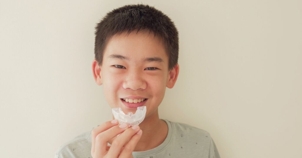 Smiling Asian preteen boy holding invisalign braces, mouthguard, teen orthodontic oral health care concept