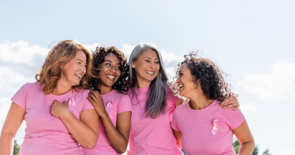 Cheerful multiethnic women with ribbons of breast cancer awareness hugging outdoors
