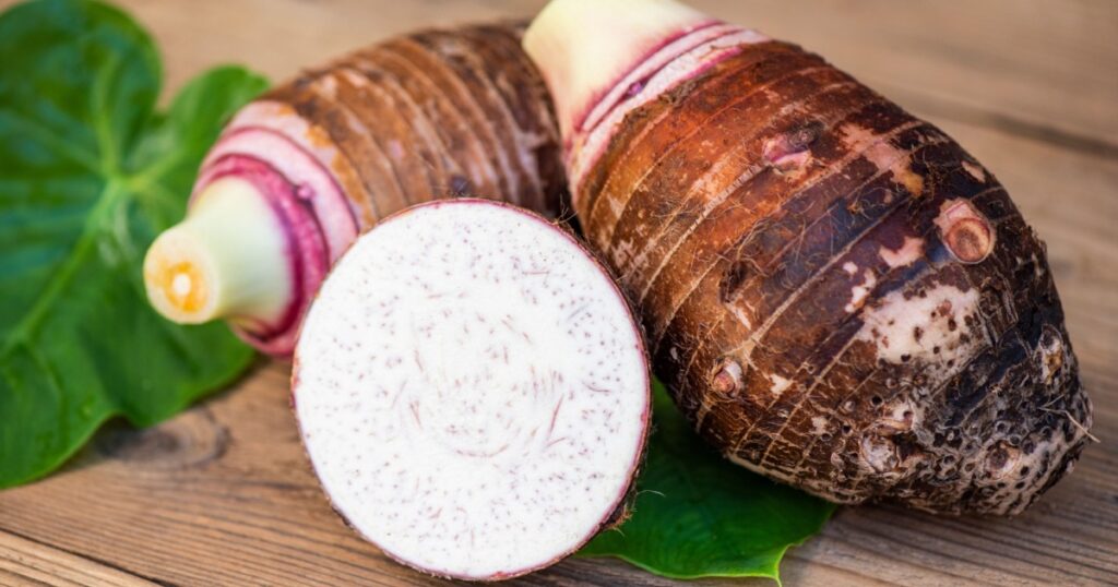 Taro root with half slice on taro leaf and wooden background, Fresh raw organic taro root ready to cook