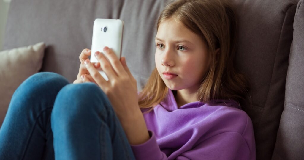 Upset depressed caucasian little kid girl holds mobile phone expresses sorrow and regret blames