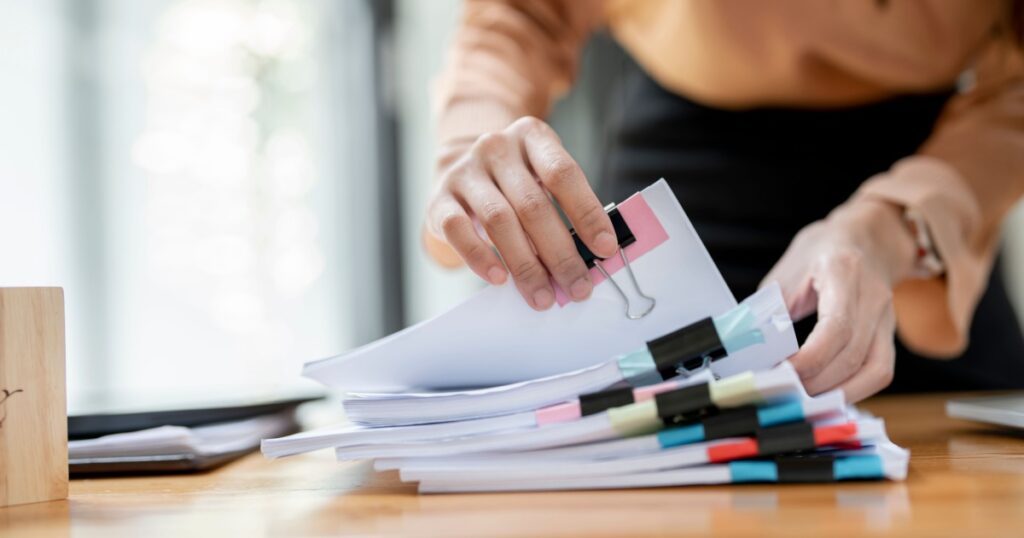 Businesswoman hands working in Stacks of paper files for searching and checking unfinished document achieves on folders papers at busy work desk office