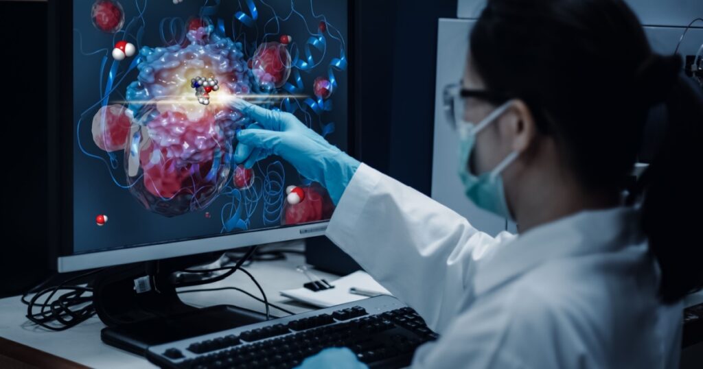 Researcher woman indicates the position of drug sample in the modelling simulation of drug development as shown on a computer monitor. The analytical computer is a supercomputer for drug simulation.
