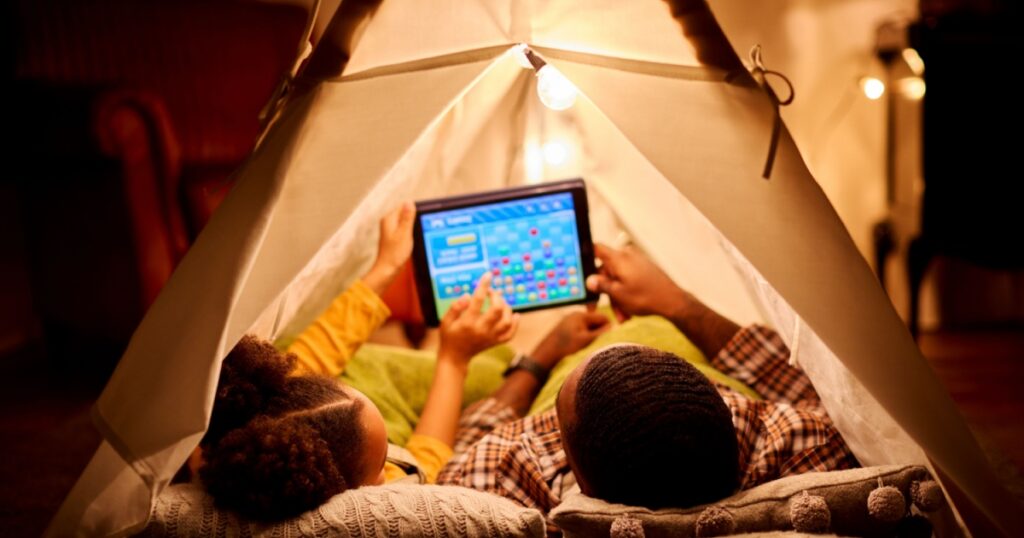 Father And Daughter At Home Lying In Indoor Tent Or Camp Gaming On Digital Tablet