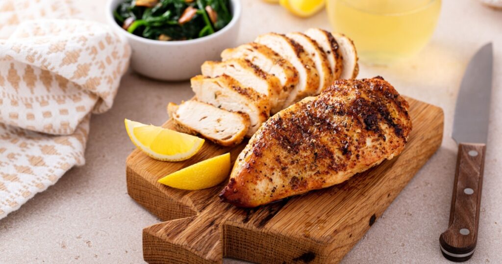 Grilled chicken breast with spice rub and lemon on a cutting board, sliced and whole