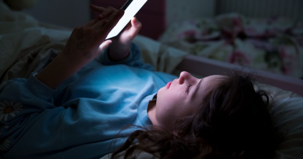 A child using smart phone lying in bed late at night, playing games, watching videos online, scrolling screen. Children's screen addiction. Child's room at night.