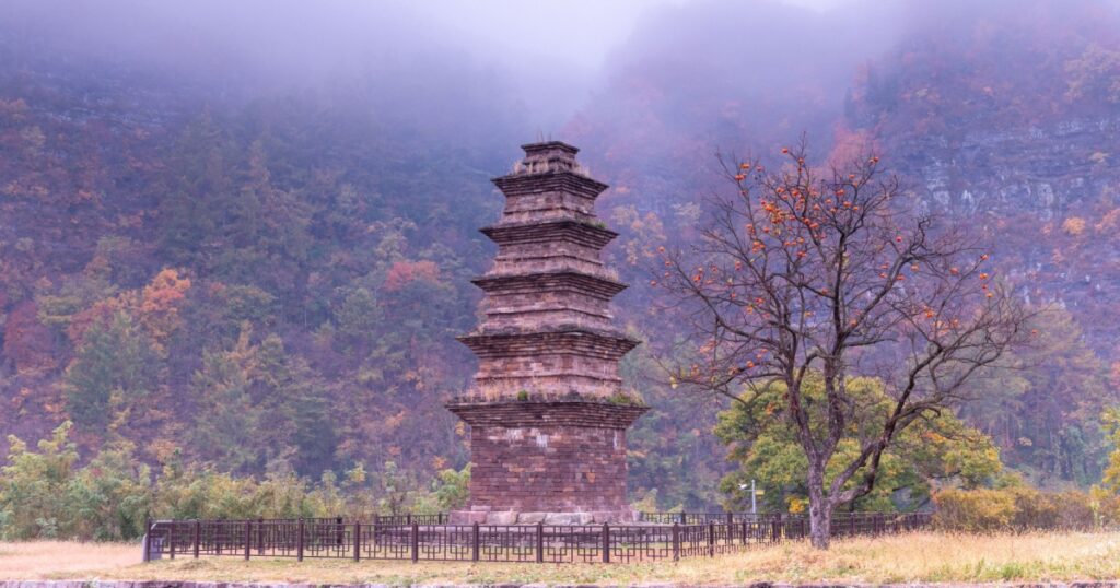 Autumnal and morning view of Hyeon five-story stone pagoda with a persimmon tree against fog on the mountain at Hyeon-ri near Yeongyang-gun, South Korea