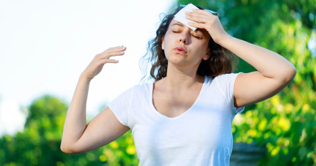 Young woman having hot flash and sweating in a warm summer day. Woman drying with paper napkin in too hot weather