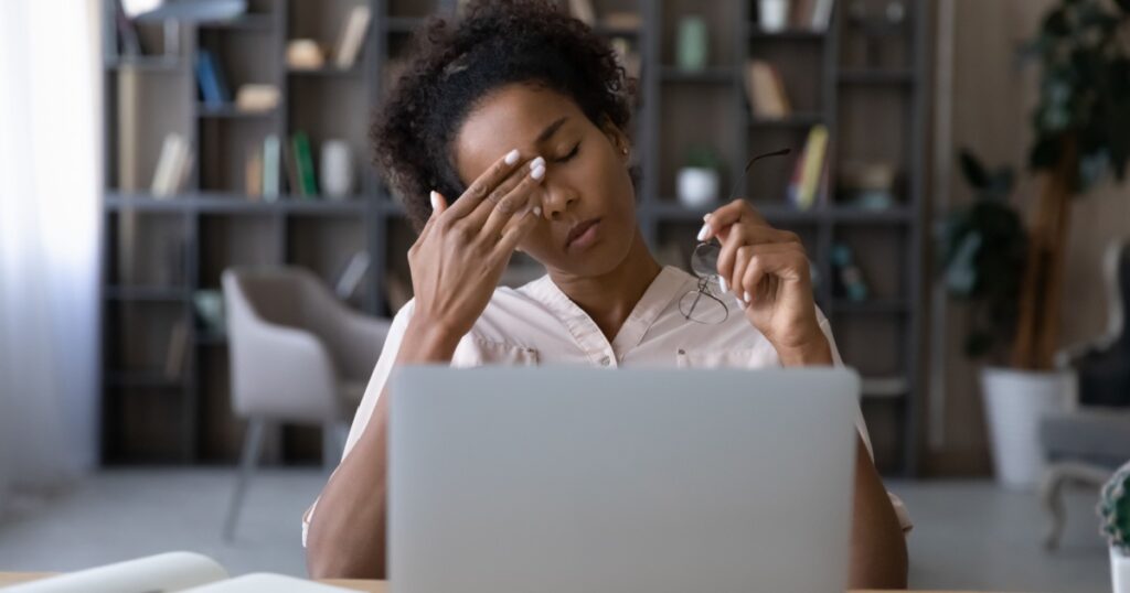 African gen Z student girl tired of studying at computer, touching irritable eyelids, face with closed eyes. Young woman holding glasses, suffering from headache, working at laptop too long