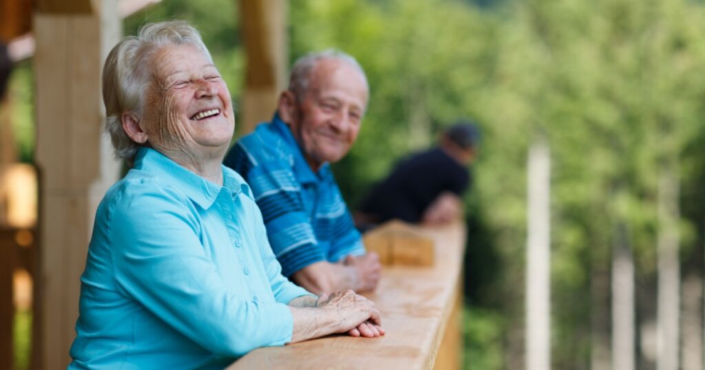 Happy senior couple looking to surroundings areas and smiling. Posing in wooden tower and watching for nature scenery in forest. Summer holidays. Blurred forest background.