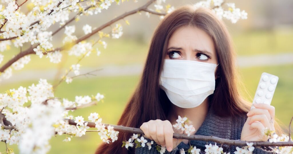 Woman with Respirator Mask Fighting Spring Allergies Outdoor - Portrait of an allergic woman surrounded by seasonal flowers wearing a protective mask