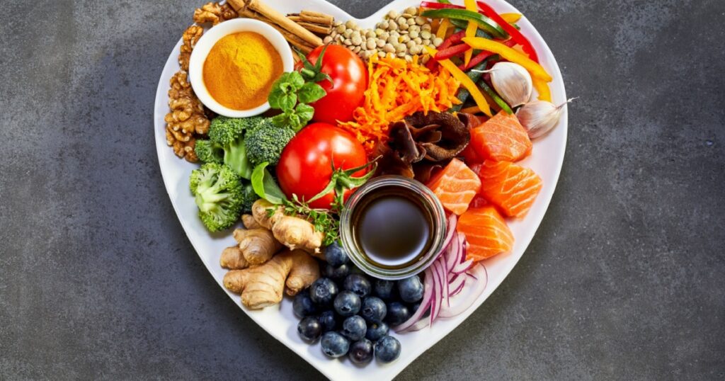 Healthy diet for the cardiovascular system with a heart-shaped plate of acai, lentils, soy sauce, ginger, salmon, carrot, tomato, turmeric, cinnamon, walnuts, garlic, peppers, broccoli, basil, onion