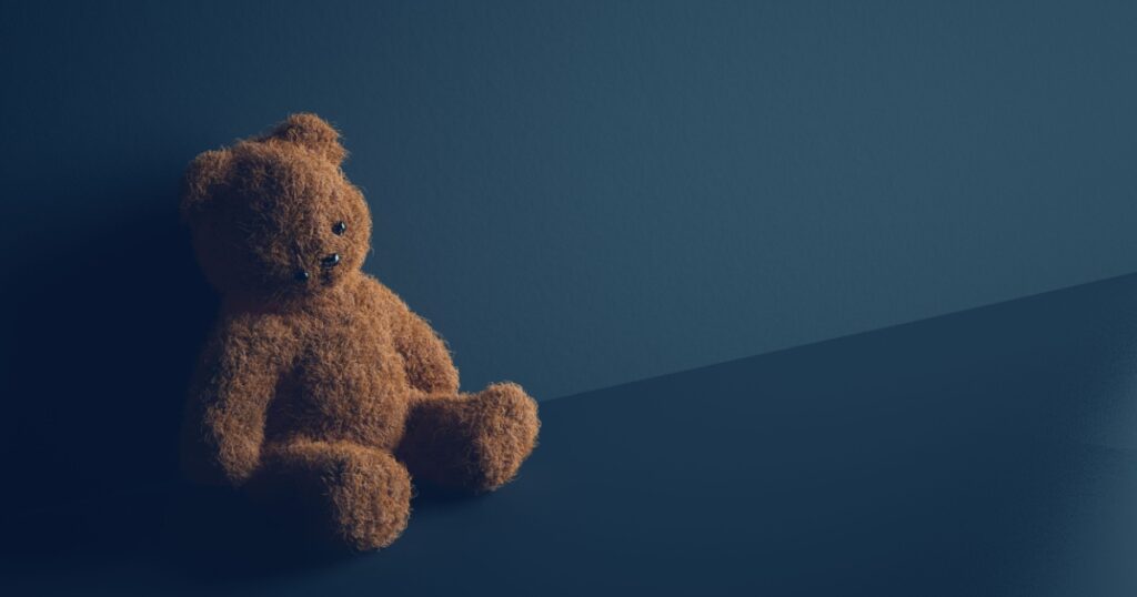 Teddy bear with torn eye sits in dark room. Child abuse and violence concept.