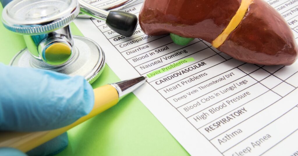Liver problems concept photo. The doctor points in diagnosis process to inscription Liver problems on a sheet of the medical history of the patient, which lies near the shape of liver and stethoscope
