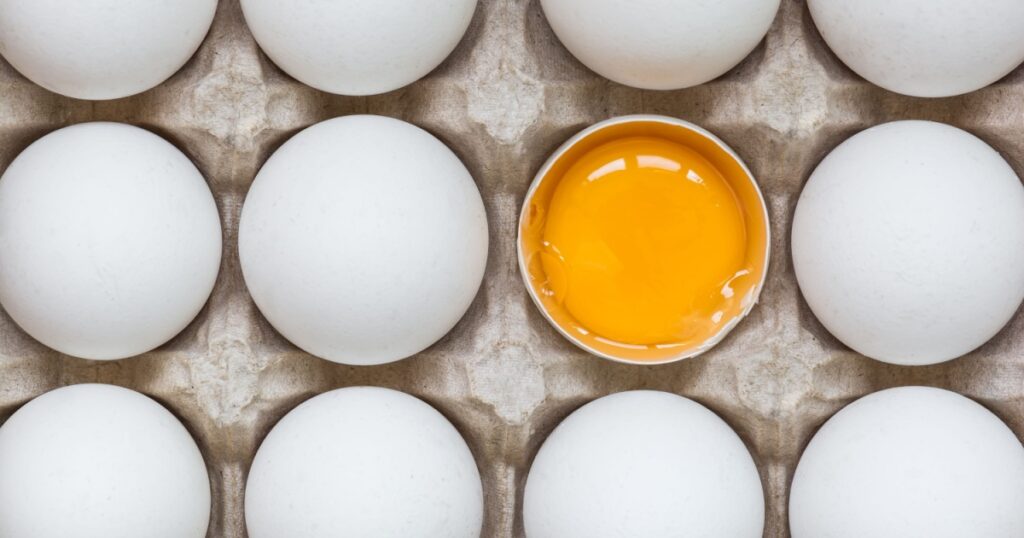 Huevo de gallina medio roto entre otros huevos.