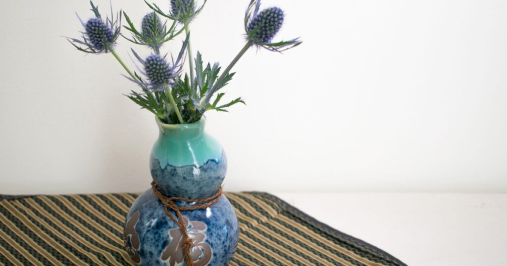 Unusual blue flowers arranged in a blue odd shaped oriental vase on top of a stripped cloth against white background.