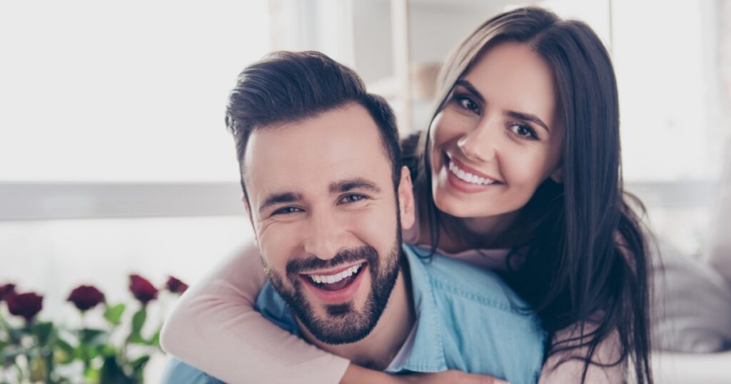 Close up photo of cheerful excited glad careless happy with toothy beaming smile brunette attractive woman and with stylish hairdo man, she is hugging him from the back