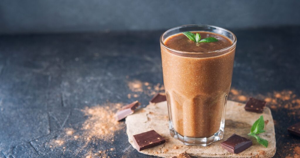 Chocolate smoothie with banana, decorated with mint leaf on the dark background with pieces of chocolate and cocoa powder. Healthy diet food. Selective focus, space for text