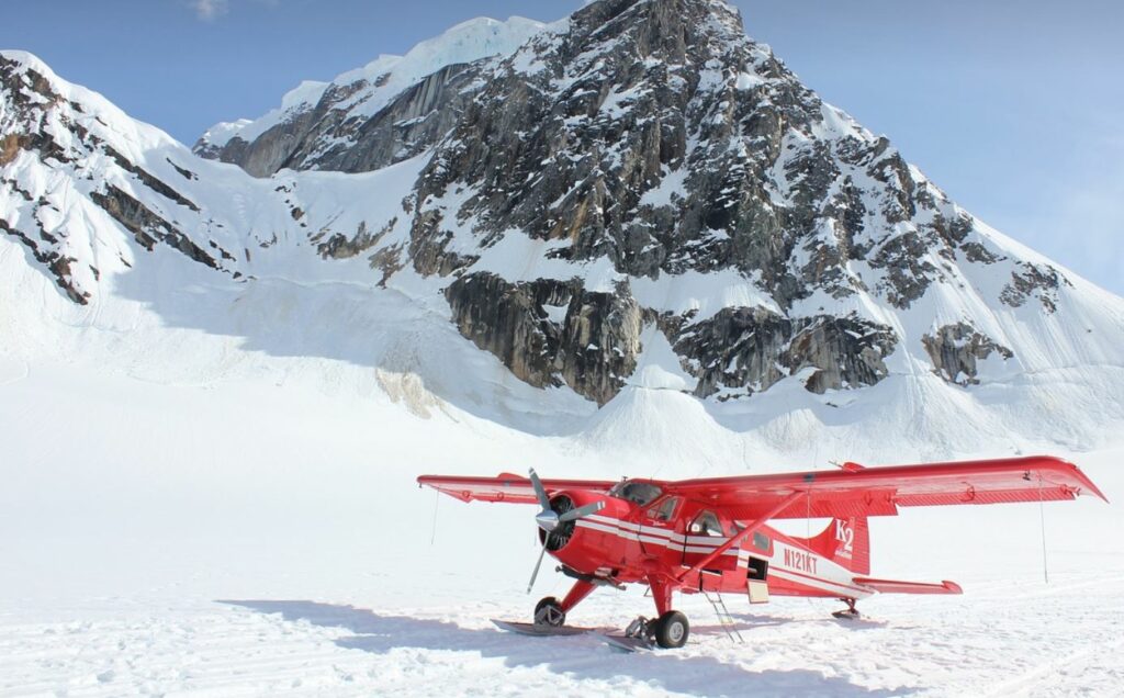 Red airplane with snowy mountain in the background. 