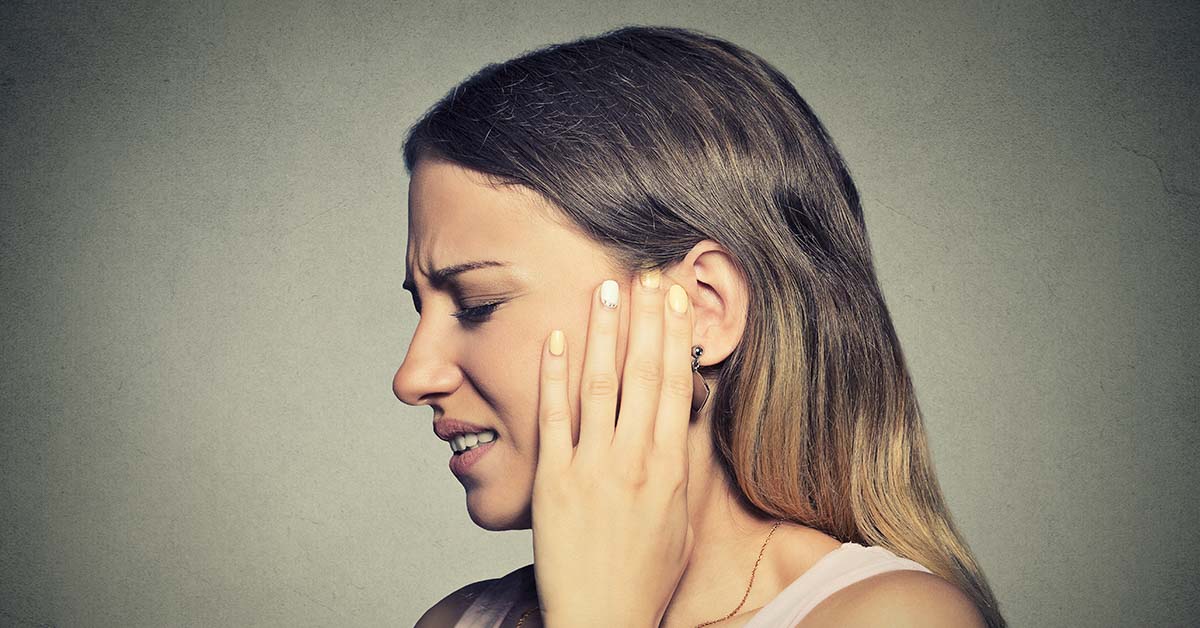 woman in pain with hand placed over ear. ear infection symptoms concept