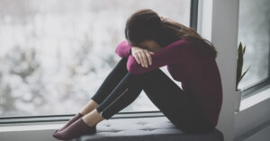 20 Common Gaslighting Phrases Used to Manipulate and Confuse You woman sitting by window ledge with face placed down over knees