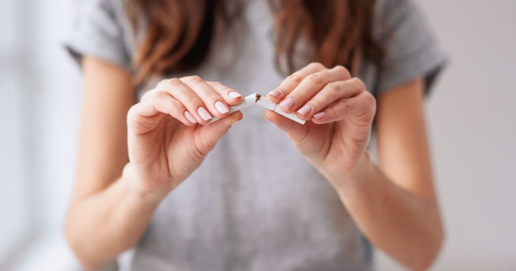 Stop smoking cigarettes concept. Portrait of beautiful smiling girl holding broken cigarette in hands. Happy female quitting smoking cigarettes. Quit bad habit, health care concept. No smoking.