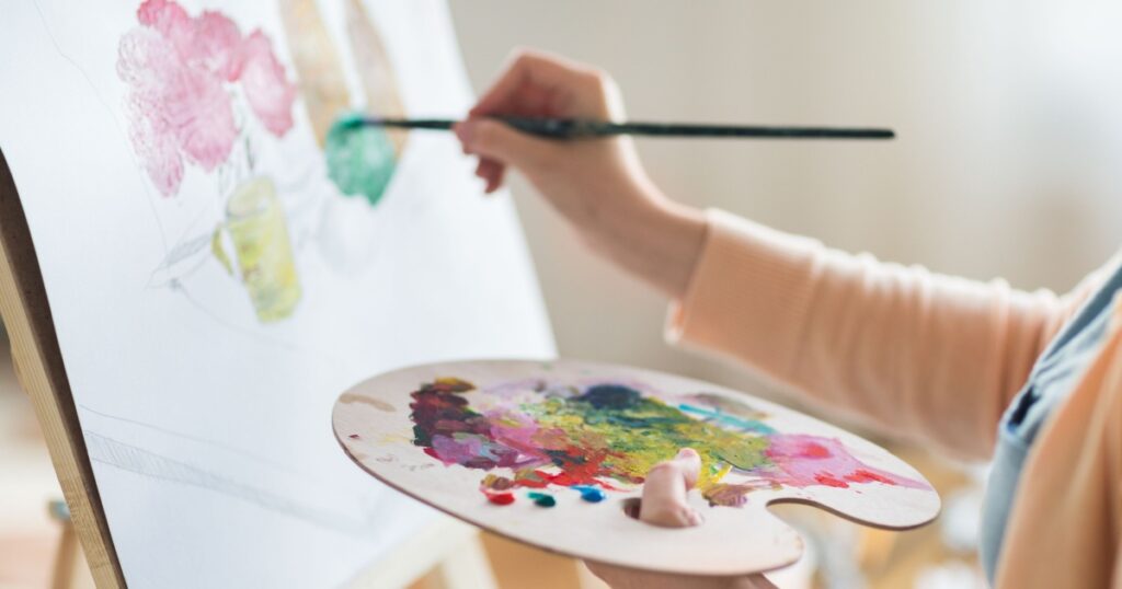 art, creativity and people concept - close up of artist with palette and brush painting still life on paper at studio