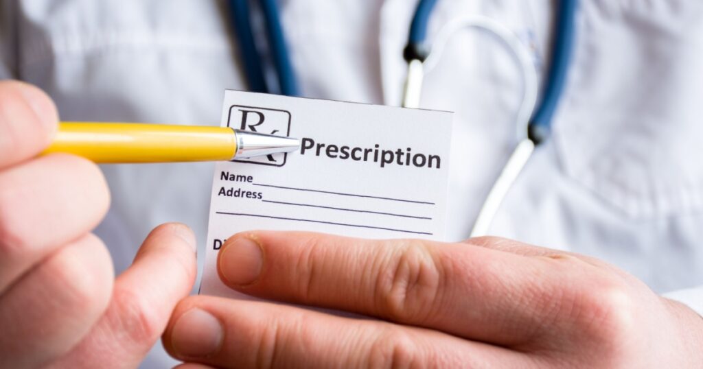 Doctor in foreground holding sample of prescription or recipe for drug, other hand indicates designation of prescription medication, which means issuing medicines by pharmacist only