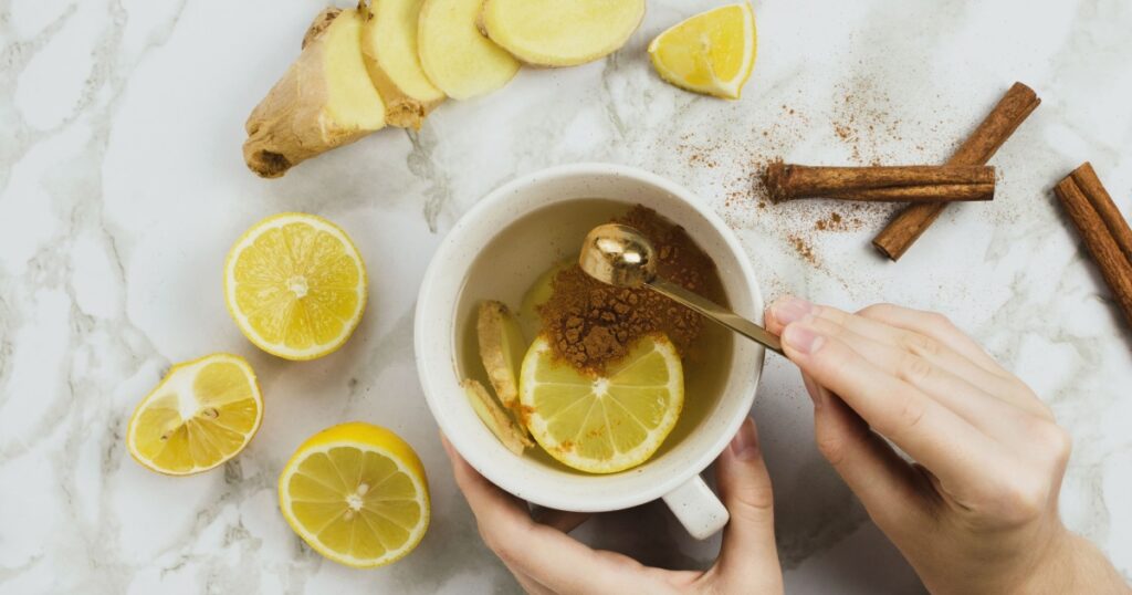 Flatlay of healthy drink with lemon, fresh ginger root, cinnamon sticks and agave syrup on marble background, natural cold or sore throat