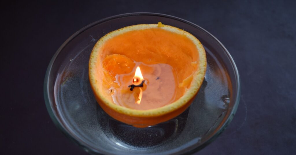 Close perspective of a half sliced orange peel floating in water with a diy candle light