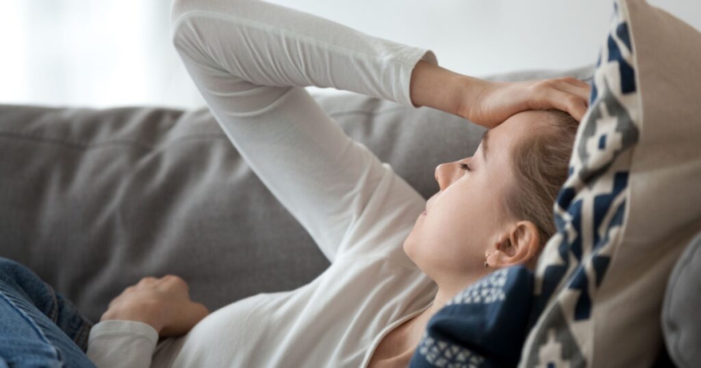 Upset depressed young woman lying on couch feeling strong headache migraine, sad tired drowsy teenager exhausted girl resting trying to sleep after nervous tension and stress, somnolence concept