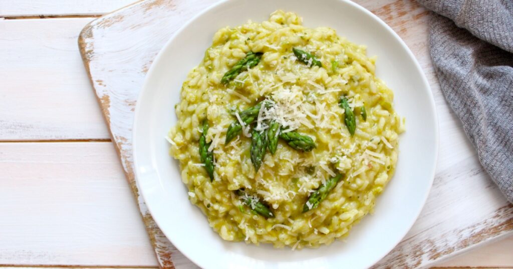 Italian risotto with spring asparagus and parmesan cheese in plate on light background. Top view with copy space.
