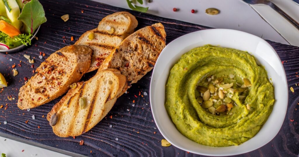 Hummus with spinach and pumpkin seeds in a bowl on a wooden board and bruschetta, oriental cuisine, horizontal orientation