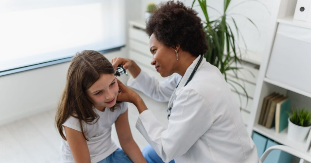 Woman afro american doctor general practitioner examining ear of a ill child. Ear infections.